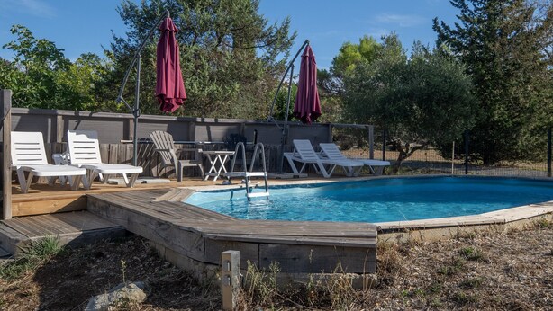Une piscine entourée d’une terrasse en bois, de chaises longues blanches et de parasols rouges.