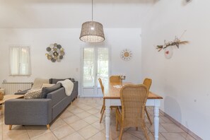 Un salon comprenant un canapé, une table à manger et des chaises, un luminaire suspendu et une porte avec des panneaux de verre.