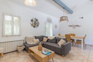 Un salon comprenant un canapé, une table basse, un panier en osier et un coin repas avec des chaises et une table.