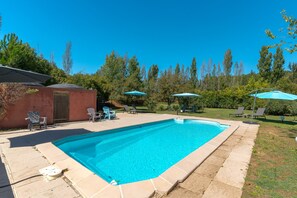 A rectangular swimming pool with a tiled edge, surrounded by a patio area with lounge chairs and umbrellas. - Domaine Plan des Devens – Peaceful 4-Star Retreat with Heated Pool (Roussillon)