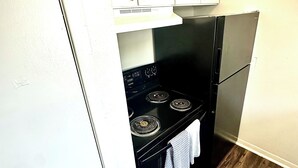 Eine kleine Küche mit weißen Schränken, einem schwarzen Herd und einem Kühlschrank.