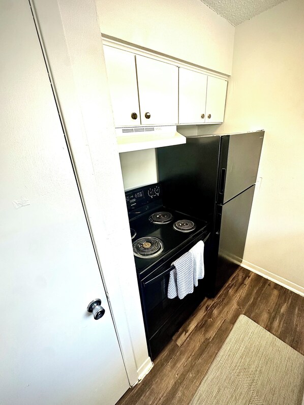 Una cocina compacta con armarios blancos, una estufa negra y un refrigerador.
