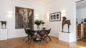 A dining area with a round table, black chairs, a large painting, and a sculpture on pedestals.