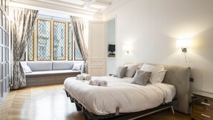 A bedroom with a bed, a window seat, and a bedside table.