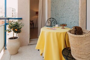 Un balcon avec une table jaune, une plante en pot, un panier en osier et un mur recouvert de carreaux.