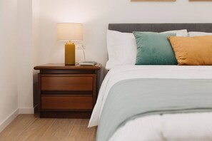 Un lit bien fait, avec des oreillers, une lampe de chevet et une table de nuit en bois dotée de tiroirs.