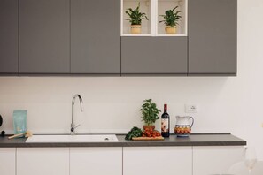 A kitchen with a sink, a countertop, and cabinets. There are potted plants on the countertop and a wine bottle.
