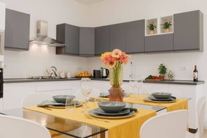 Une cuisine moderne avec des meubles gris, une table à manger dressée pour quatre personnes et un vase rempli de fleurs.