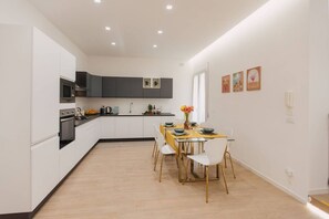 A modern kitchen with white cabinets, a dining table with chairs, and a small island with a sink. - Elegant apartment in the heart of Syracuse, 3 bedrooms and 3 bathrooms, city center. (SIRACUSA)