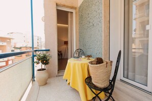A balcony with a yellow table, a chair, a potted plant, and a wicker basket.