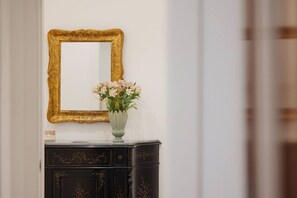 A mirror with a gold frame, a vase with flowers, and a black cabinet with gold detailing. - Elegant apartment in the heart of Syracuse, 3 bedrooms and 3 bathrooms, city center. (SIRACUSA)