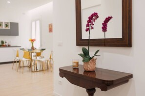 A modern interior with a dining area, a wooden console table with a vase and candle, and a framed orchid painting on the wall.