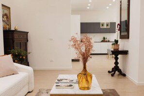 Un salon avec un canapé, une table basse surmontée d’un vase, et une cuisine en arrière-plan.