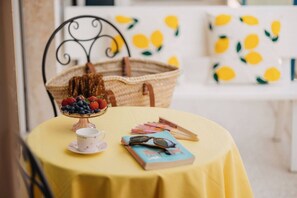 Uma mesa com toalha amarela, cesto de vime, tigela de frutas, um livro e um par de óculos.