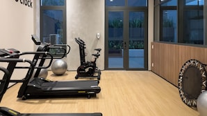 Un gimnasio con equipo de ejercicio, ventanas amplias y suelo de madera.