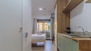 Habitación de hotel compacta con cama, kitchenette y vistas al balcón exterior a través de una puerta corrediza.