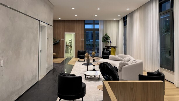 Una sala de estar moderna con un sofá blanco, sillas negras, una mesa de centro de madera y un amplio ventanal con cortinas.