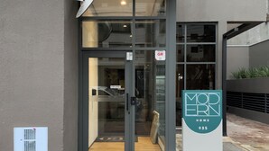 Entrada de un edificio moderno con puerta de vidrio, letrero de seguridad y felpudo con la palabra "OLO".