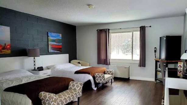 Habitación de hotel con dos camas, televisión, escritorio, silla y ventana con cortinas.