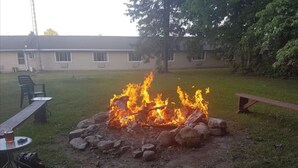 Un patio trasero con un hoyo de fuego rodeado de rocas, una mesa de picnic y una silla de descanso.