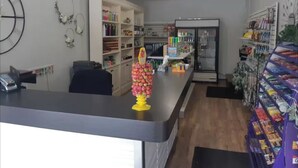 Un área de recepción con mostrador, estanterías con diversos objetos, un reloj y un ventilador de techo.