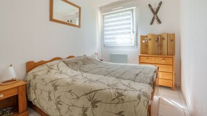 Un dormitorio con cama, cómoda de madera, espejo y ventana con persianas.