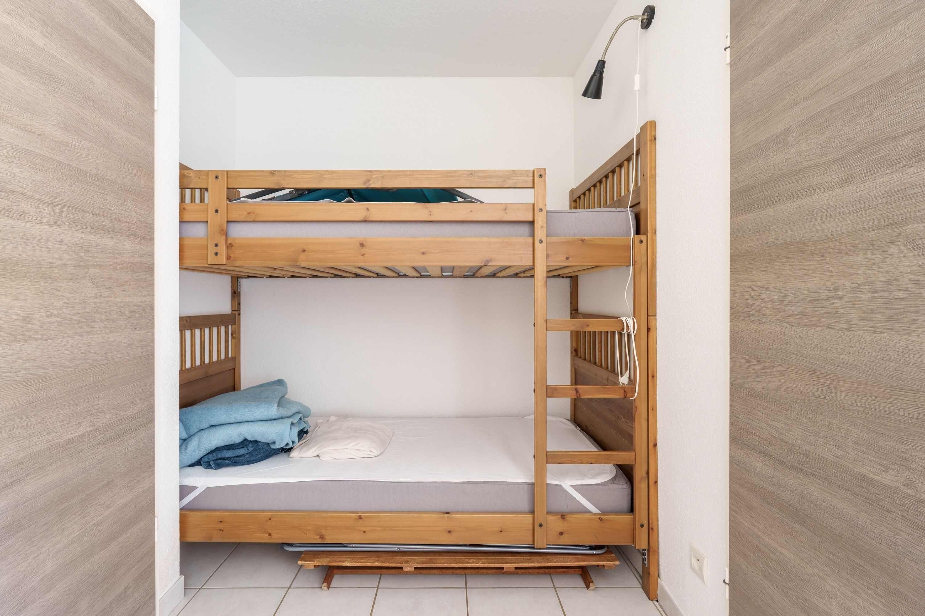 Une chambre avec un lit superposé en bois, un matelas et une couverture.