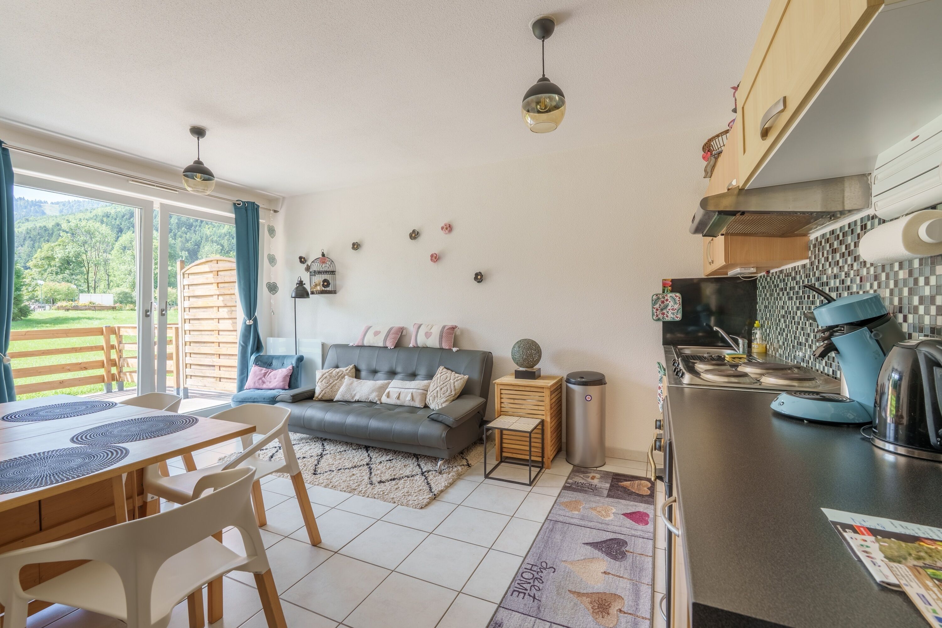 A modern kitchen with a dining area, a sofa, and a view of a wooden deck.