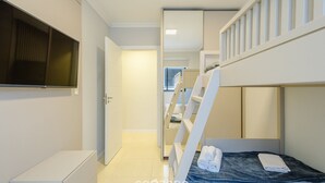 Quarto de hotel moderno com beliche, TV de tela plana, guarda-roupa e cama bem arrumada.