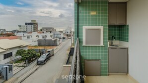 Varanda residencial com vista para a cidade, parede revestida e pequena cozinha.