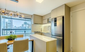 A modern kitchen with a built-in refrigerator, a gas stove, and a large window offering a city view. - Apto prox. do mar em Balneário Piçarras PDG0202 (Picarras)