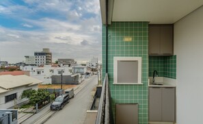 A residential balcony with a view of a cityscape, a tiled wall, and a small kitchen area. - Apto prox. do mar em Balneário Piçarras PDG0202 (Picarras)