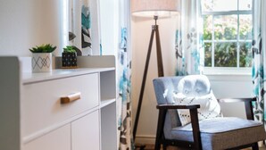 A room with a white dresser, a chair with a cushion, a floor lamp, and a window with curtains. - EV charger & desk+monitor! 2-1 in the Heights. FULLY fenced in. 5 min to d-town (Houston)