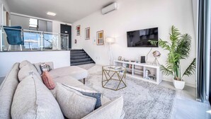 A modern living room with a sofa, a coffee table, a TV, and a staircase leading to an upper floor.