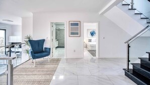 A modern living room with a blue armchair, a staircase, and a view into the kitchen.