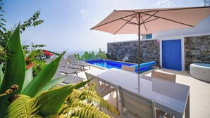 A poolside area with a table, chairs, and an umbrella. There is a stone wall and a blue door in the background.