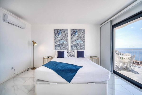 A modern bedroom with a large bed, a view of the sea, and artwork on the wall.