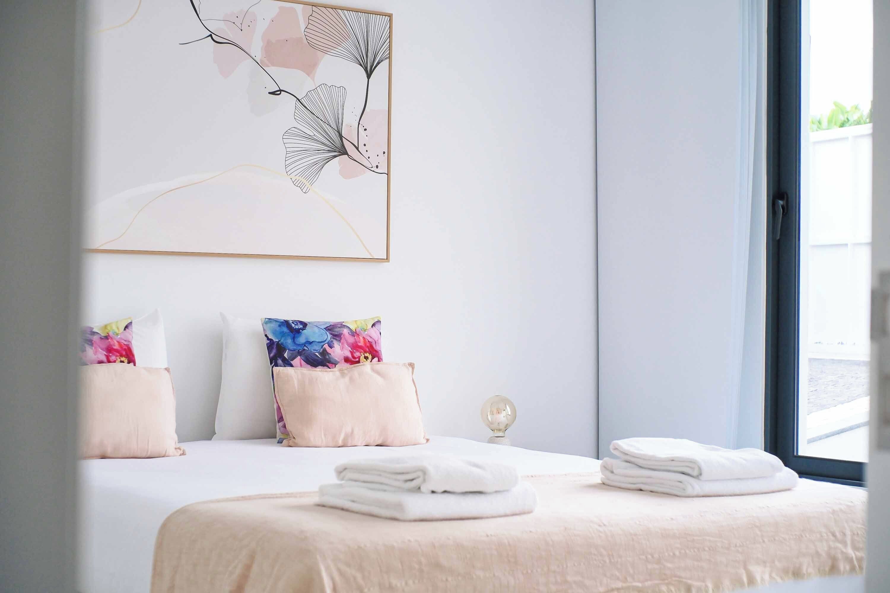 Habitación de hotel con cama, almohadas, una obra de arte en la pared y una ventana.