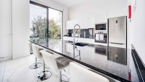 A modern kitchen with a large window, white cabinets, stainless steel appliances, and a marble countertop. - Casa das Flores - Three Bedroom Villa, Sleeps 6 (Calheta)