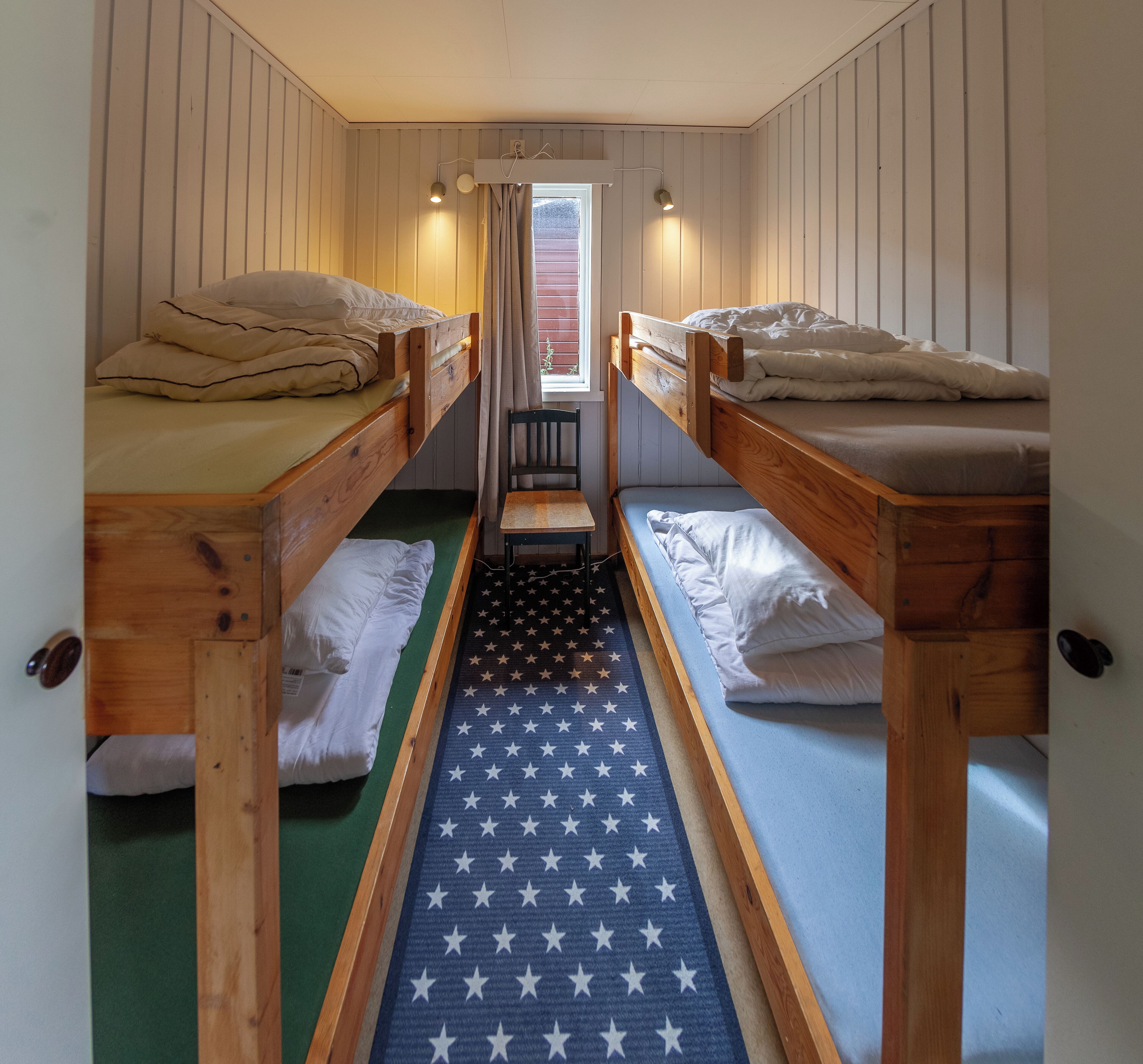 A room with two bunk beds, a small table, and a window with curtains.