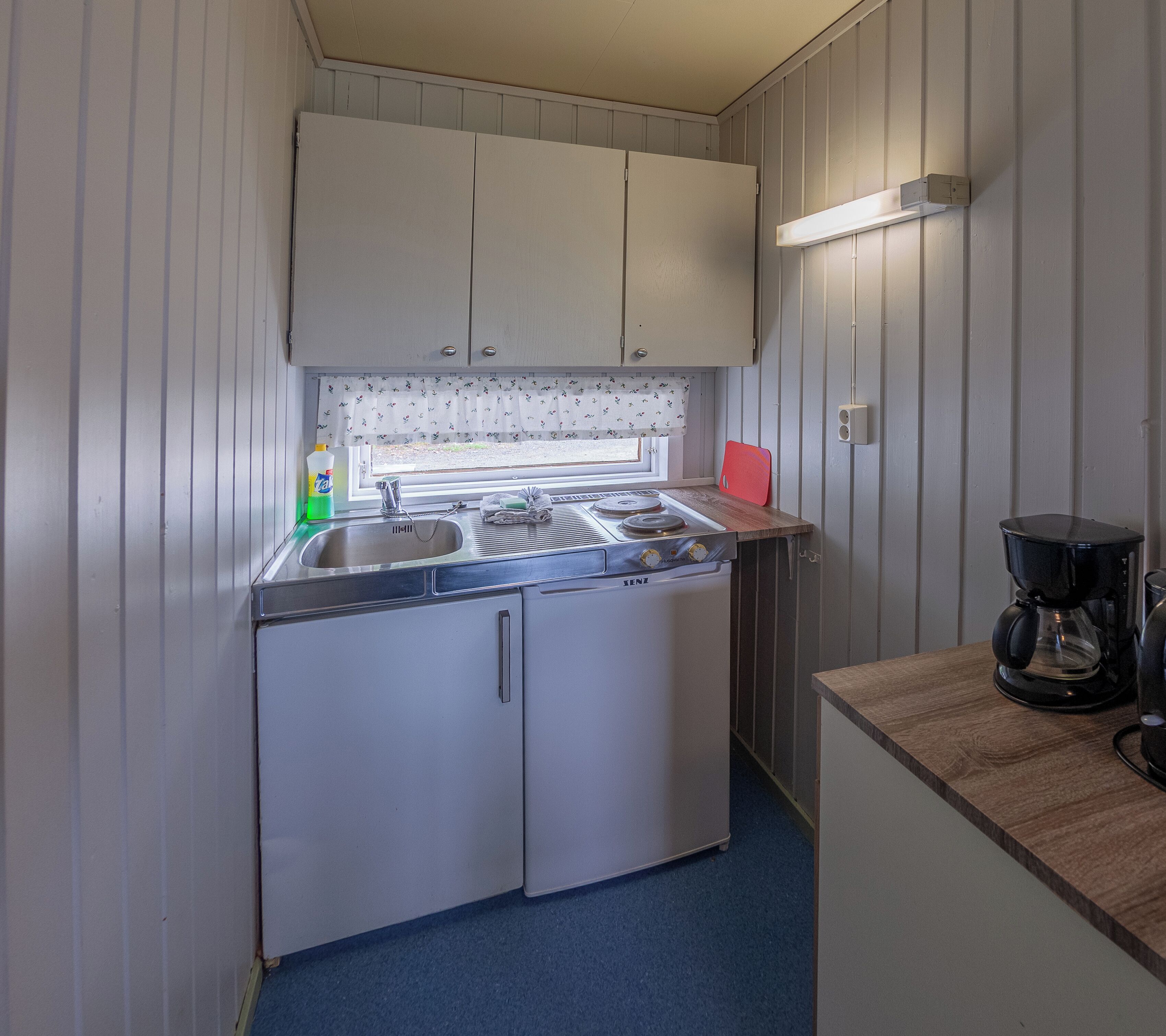 A compact kitchen with a stove, sink, and a coffee maker.