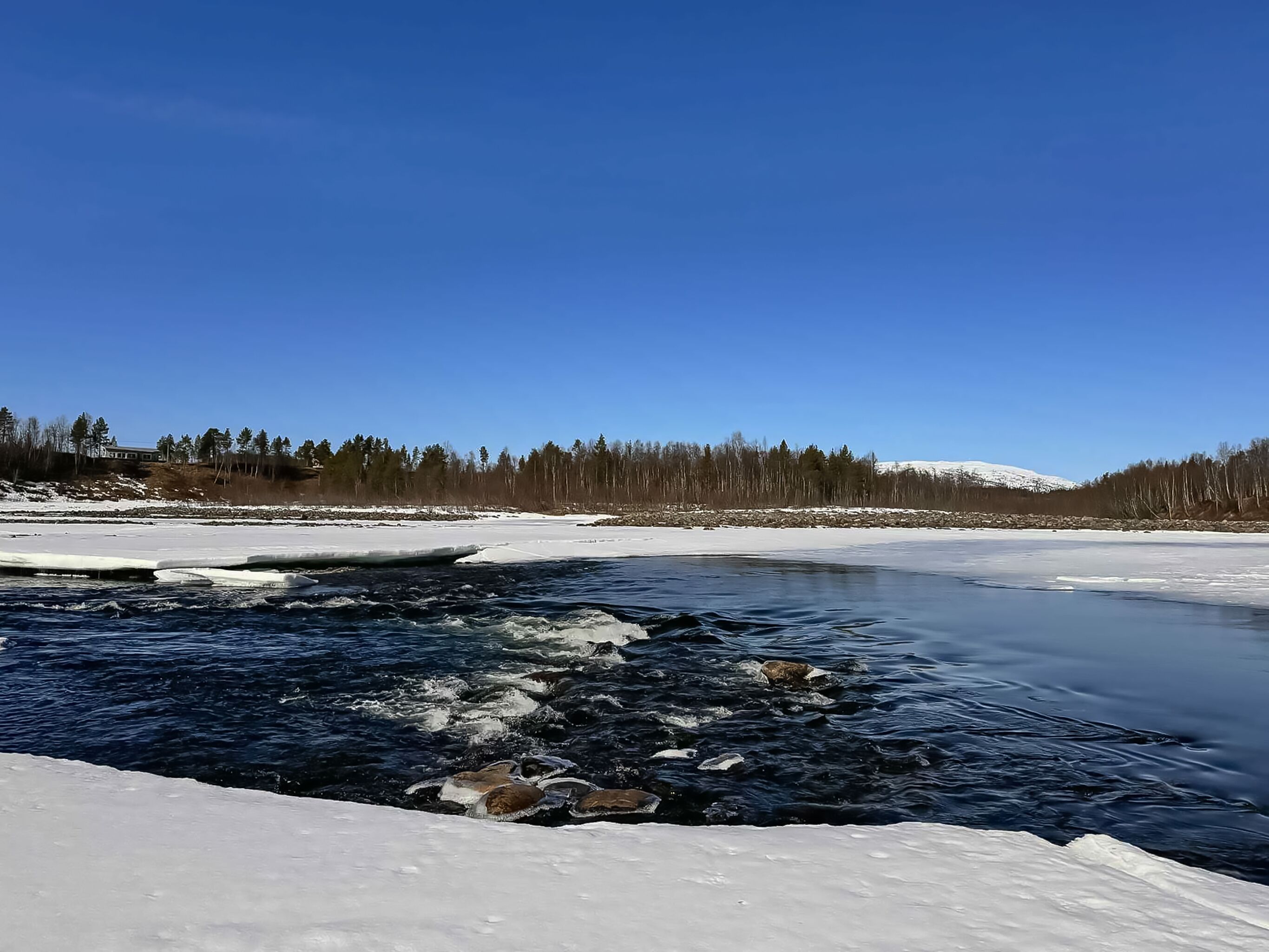 Une rivière gelée, aux rives enneigées, avec des arbres en arrière-plan.