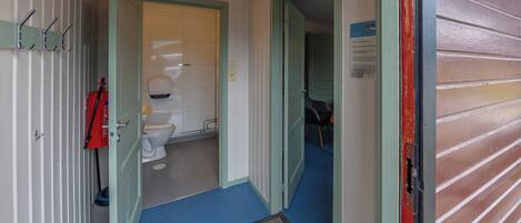 A hallway with a blue carpet, a door leading to a room with a toilet and a sink, and a fire extinguisher on the wall.