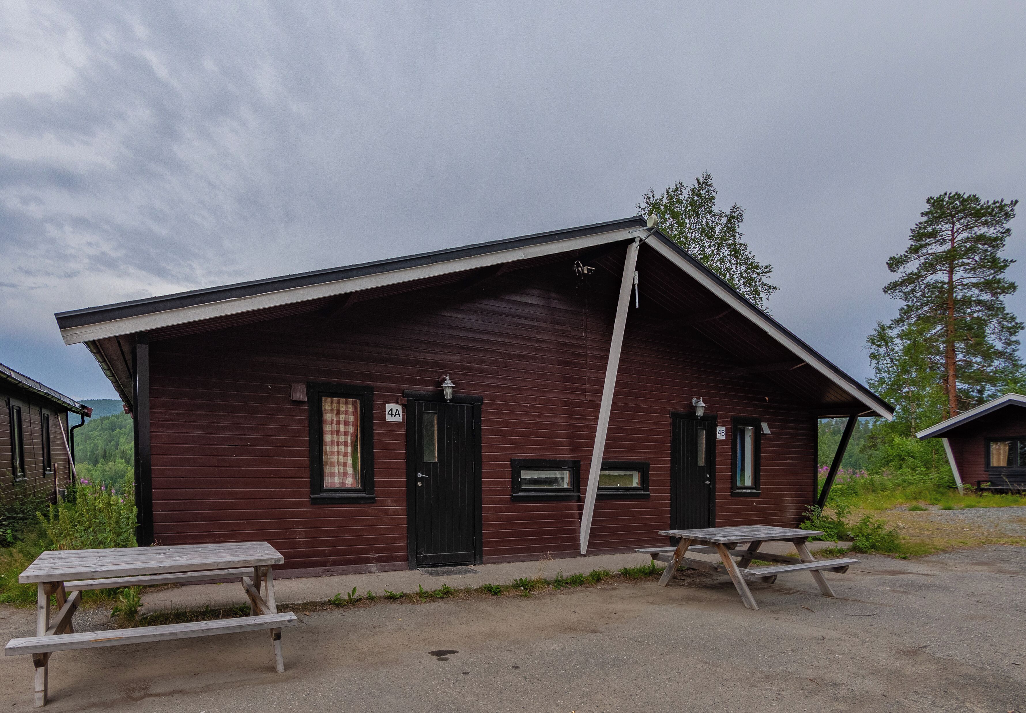 Une cabane rustique avec un toit en pente, deux fenêtres et une porte. On y trouve des tables de pique-nique à l’extérieur.