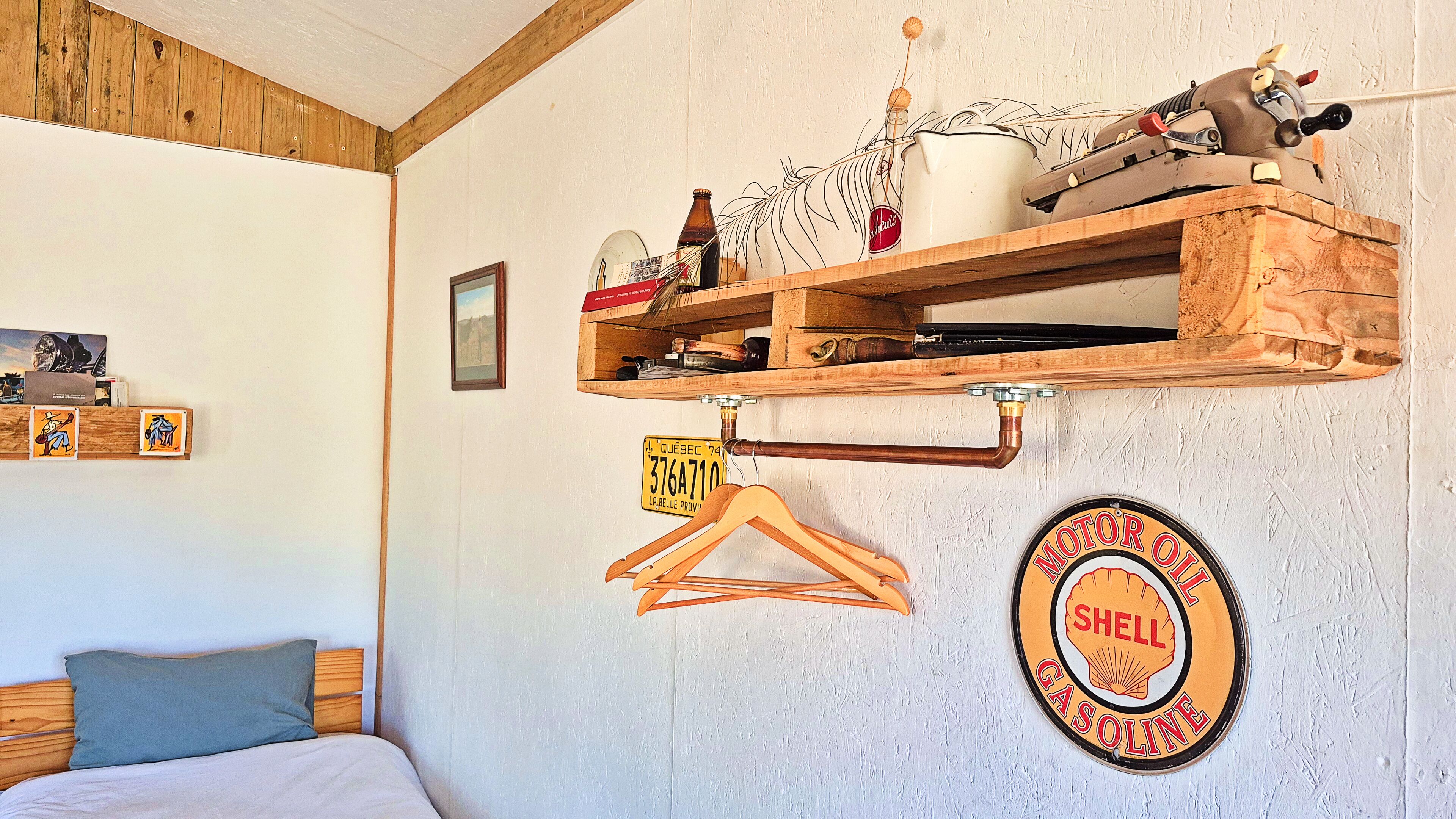 A room with a bed, wooden shelves with various items, a sign with a vehicle license plate, and a Shell gasoline sign.