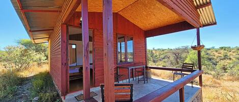 Una cabaña de madera con balcón, comedor y vistas del paisaje circundante.