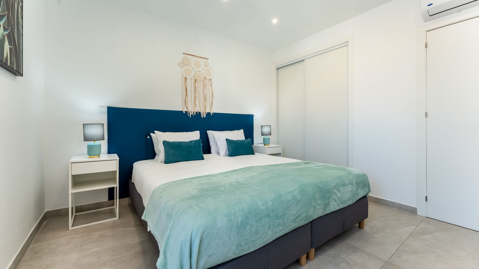 Un dormitorio moderno con una cama grande, dos mesitas de noche, aire acondicionado de pared y una puerta.