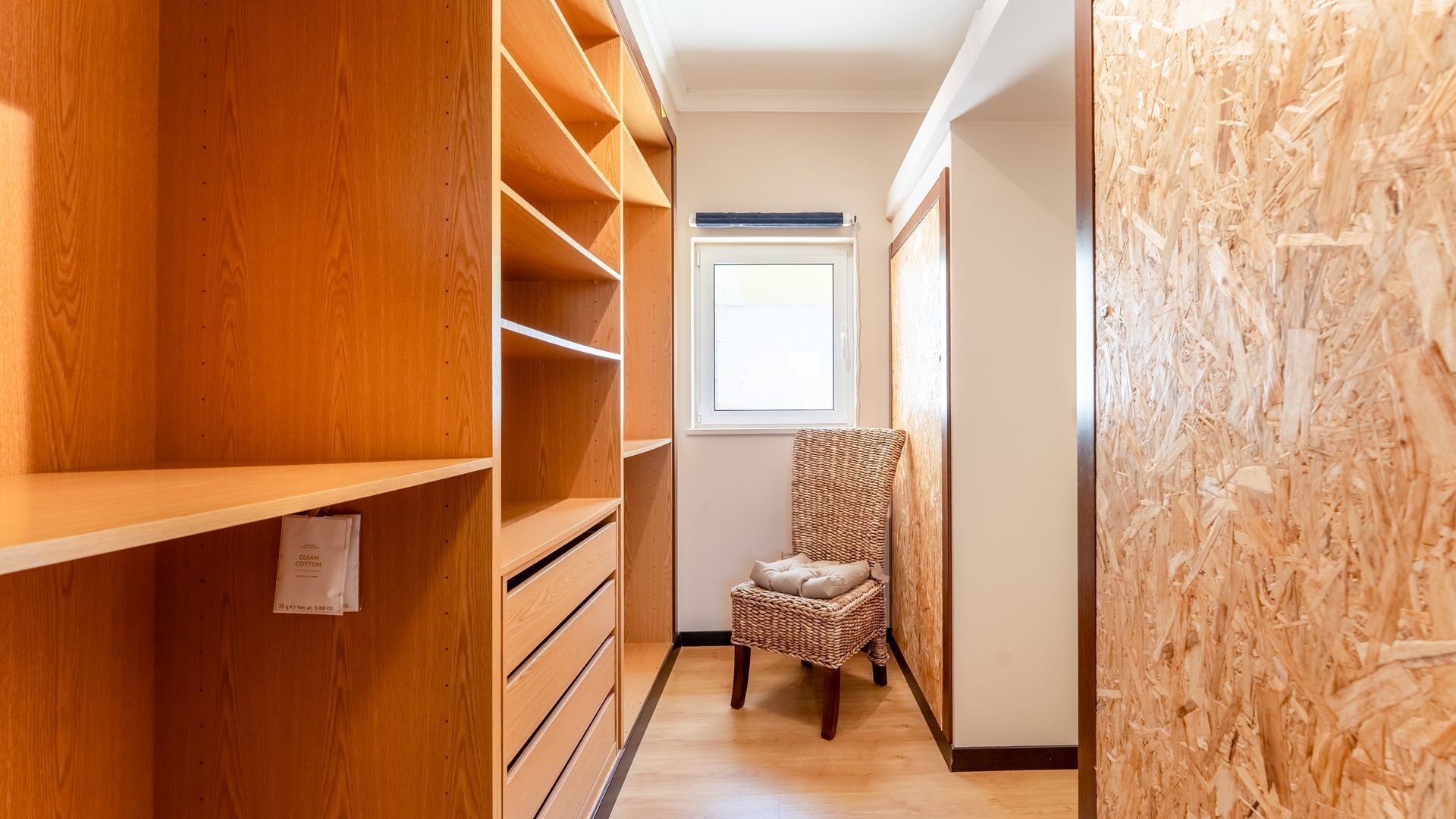 A narrow hallway with wooden shelving units on one side and a wicker chair in the center.