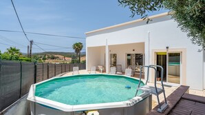 A swimming pool with a hot tub, a covered patio with chairs, and a view of the surrounding landscape.