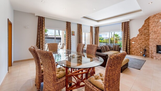 A spacious living area with a glass-top dining table surrounded by wicker chairs, a sofa, and a stone accent wall.